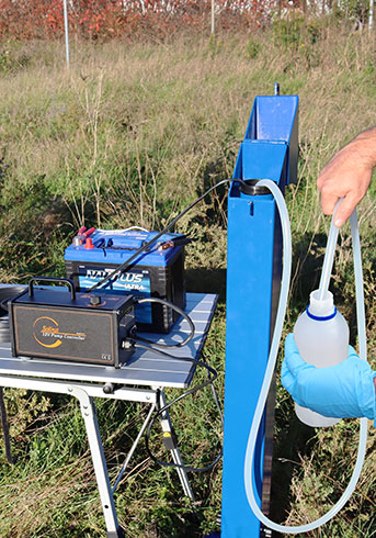 personne sur le terrain prélevant des échantillons d'eau souterraine à l'aide d'une pompe submersible solinst 12v au puits de surveillance des eaux souterraines